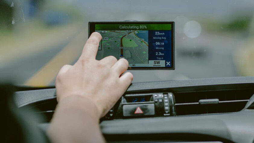 Hand touching a GPS navigation screen in a BND Car Hire vehicle, plotting a route for safari across Southern Africa.