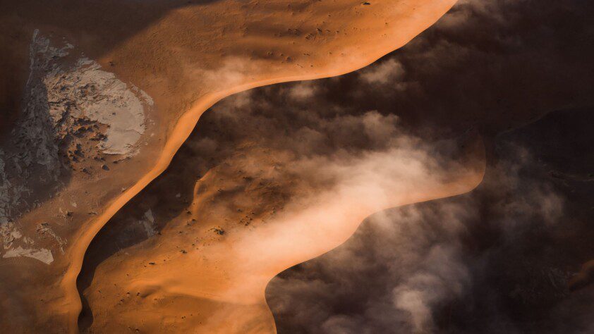 Aerial view of a winding desert river with rising mist, a prime spot for camping in Namibia.