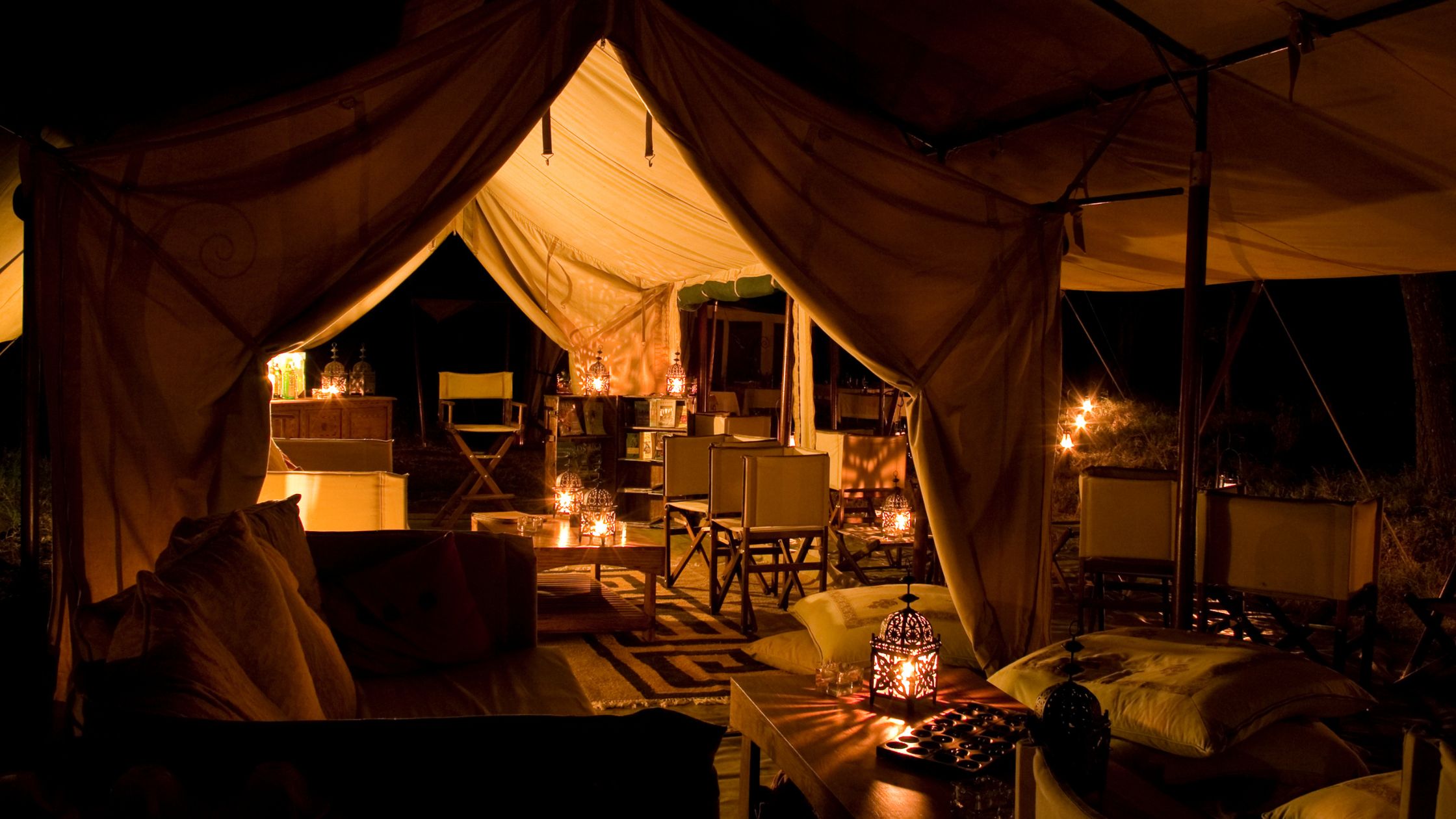 A luxurious tented camp lit by warm lanterns at night, set up for a self-drive safari experience.