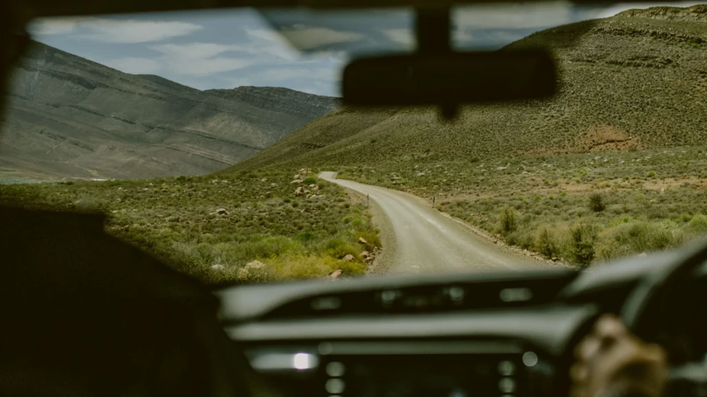 View from inside a vehicle on a safari drive, showcasing a winding gravel road through a hilly, arid landscape.