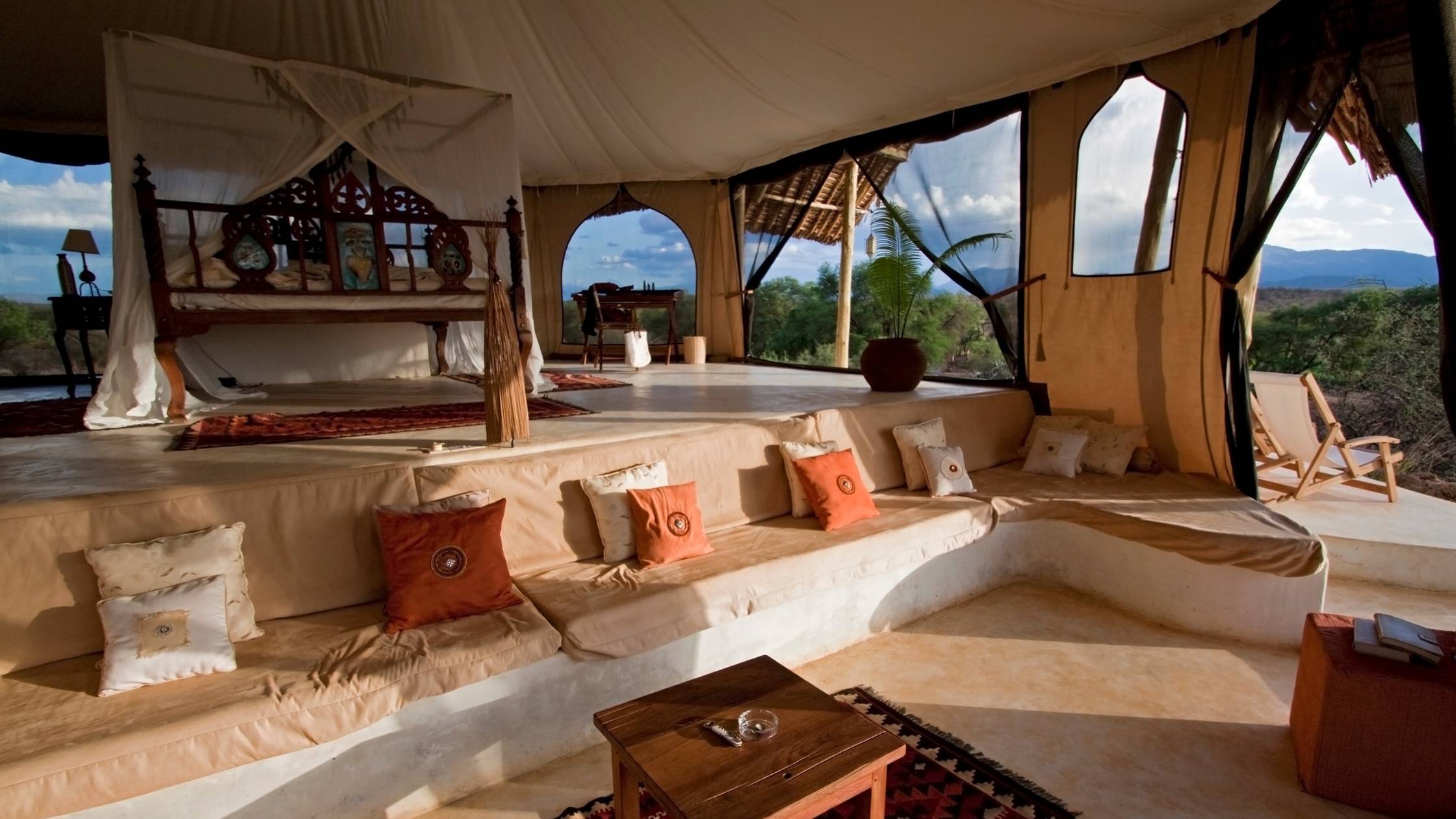 Luxury tent interior with wooden bed, cushions, and scenic views for a safari in Africa.