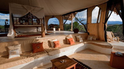 Luxury tent interior with wooden bed, cushions, and scenic views for a safari in Africa.
