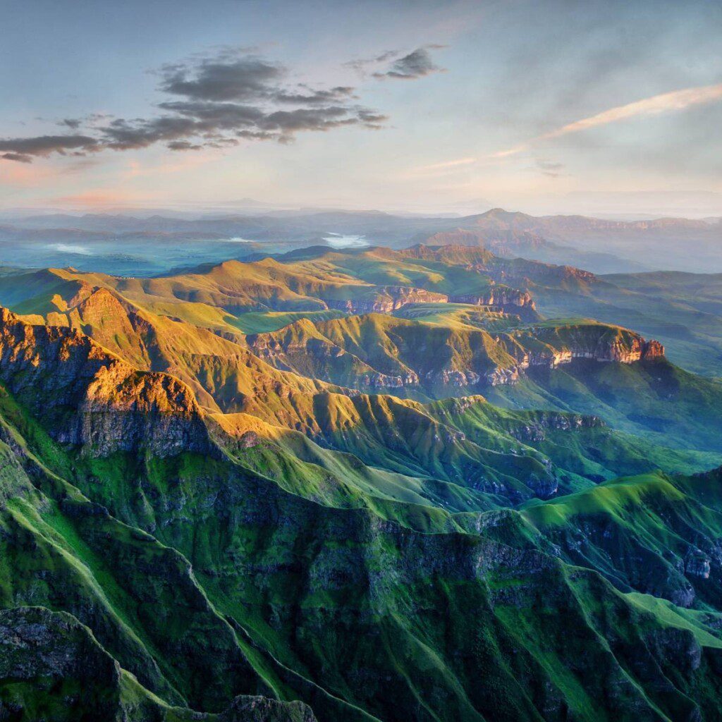 Scenic view of the Drakensberg Mountains at sunrise, showcasing lush green valleys and rugged peaks.