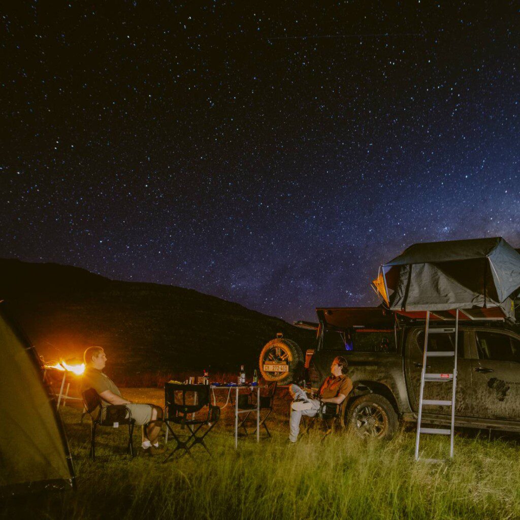 A serene night camping under a starlit sky in South Africa, with a 4x4 vehicle parked nearby, perfect for overlanding adventures.