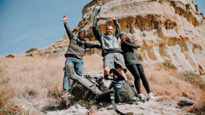 A group of three adventurers preparing for rock climbing during their overland travel in Africa, surrounded by rugged terrain.