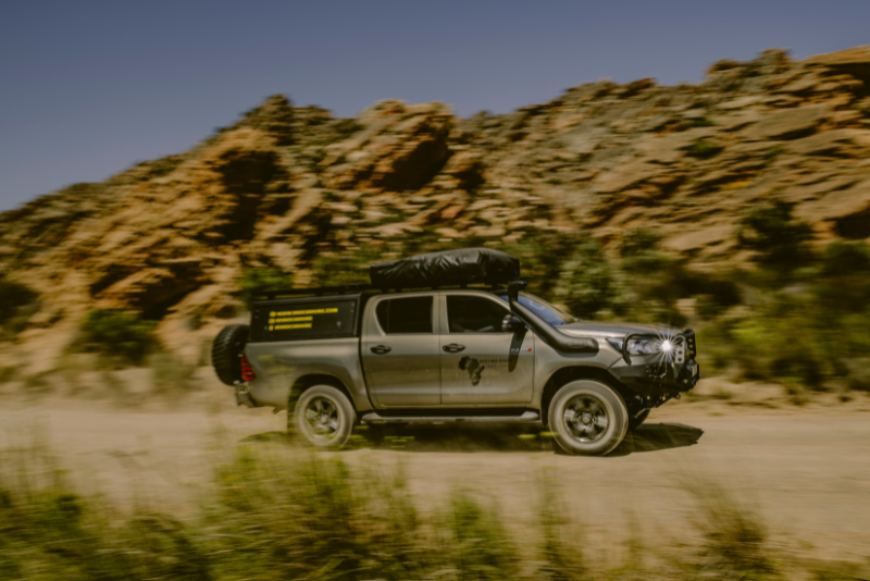 A custom-built 4x4 car hire in Botswana driving on a rugged dirt road with rocky landscapes in the background, ideal for adventurous safaris.